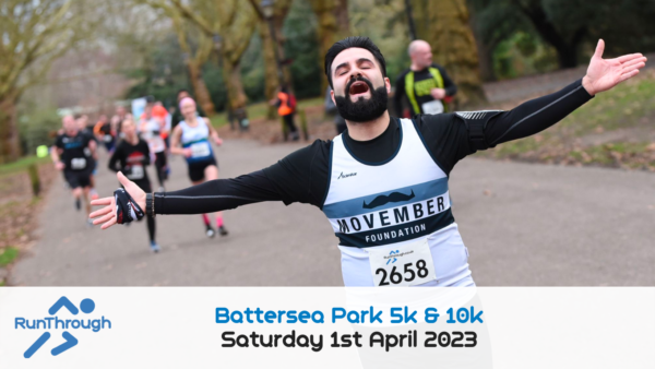 A runner with a beard and mustache wearing a Movember Foundation shirt and bib number 2658 spreads his arms wide in joy while participating in the Battersea Park 5k & 10k race on Saturday, April 1st, 2023. Other runners are visible in the background.