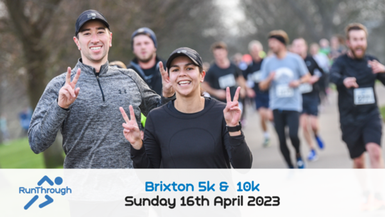 Two smiling runners gesture with peace signs while taking part in a road race. Other participants are visible in the background. The photo includes a banner with the text "Brixton 5k & 10k, Sunday 16th April 2023" and a RunThrough logo on it.