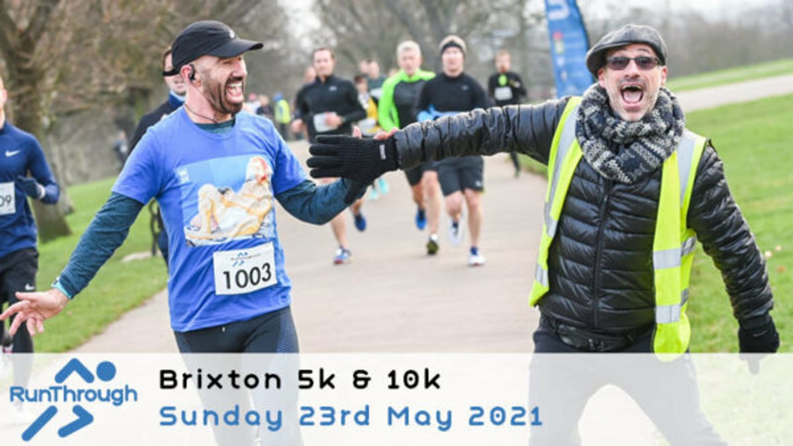 A man in a blue shirt and black cap smiles while running a marathon, reaching out to a cheering, smiling man in a yellow safety vest and hat. Other runners are visible in the background. A banner reads "Brixton 5k & 10k Sunday 23rd May 2021.