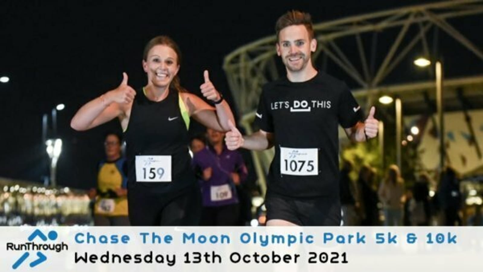 Two runners smile and give thumbs up during the Chase The Moon Olympic Park 5k & 10k event held on Wednesday, October 13th, 2021. A woman on the left wears bib number 159, and a man on the right wears bib number 1075 with a "LETS DO THIS" shirt.