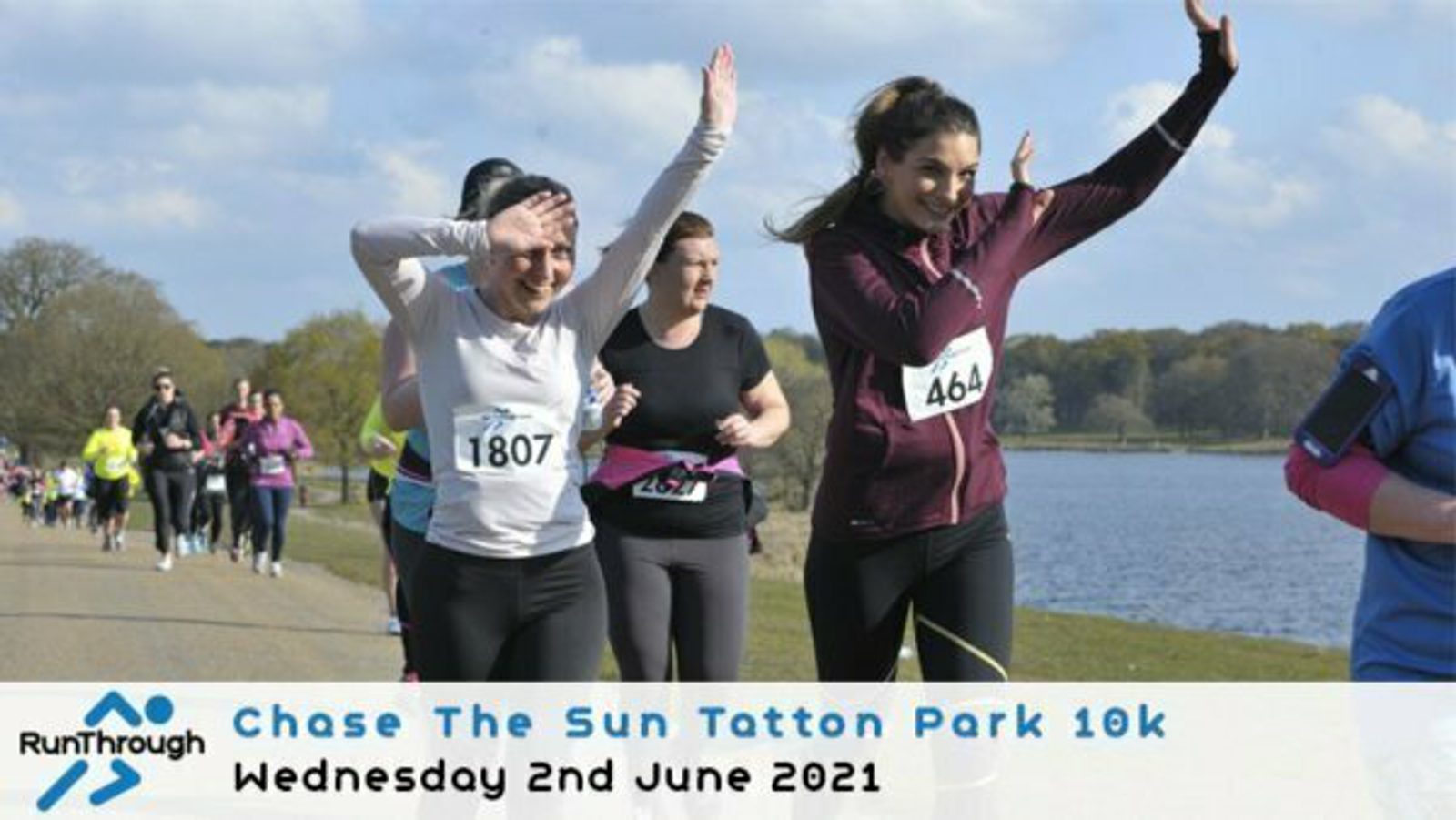 A group of runners, predominantly women, participate in the "Chase The Sun Tatton Park 10k" on a sunny day, with a lake and trees in the background. Two women in the foreground wear race numbers 1807 and 464, smiling and raising their arms as they run. The event logo and date "Wednesday 2nd June 2021" are displayed at the bottom.