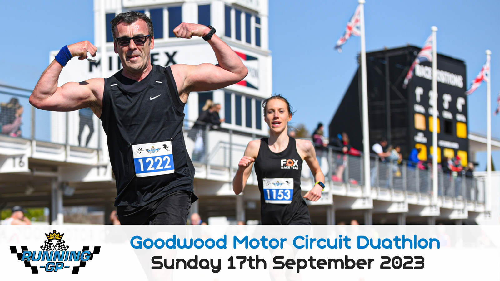 Two athletes, a man and a woman, running in a duathlon at Goodwood Motor Circuit. The man in front flexes his biceps while smiling, wearing bib number 1222. The woman behind, wearing bib number 1153, also smiles. Event signage in the background reads "Sunday 17th September 2023.