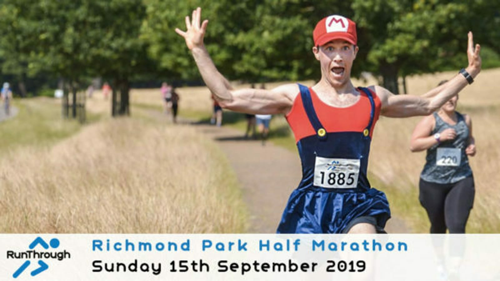 A runner in a Mario costume joyfully raises his arms as he runs along a path during the Richmond Park Half Marathon. Other runners are visible in the background. The event details read: "Richmond Park Half Marathon, Sunday 15th September 2019".