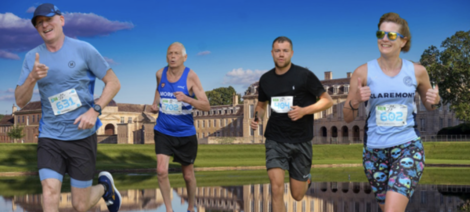 Four runners are participating in a race outdoors. Two men and one woman wear blue bibs, and one man wears a black bib. They run alongside a large historic building under a blue sky with scattered clouds. The participants appear focused and determined.