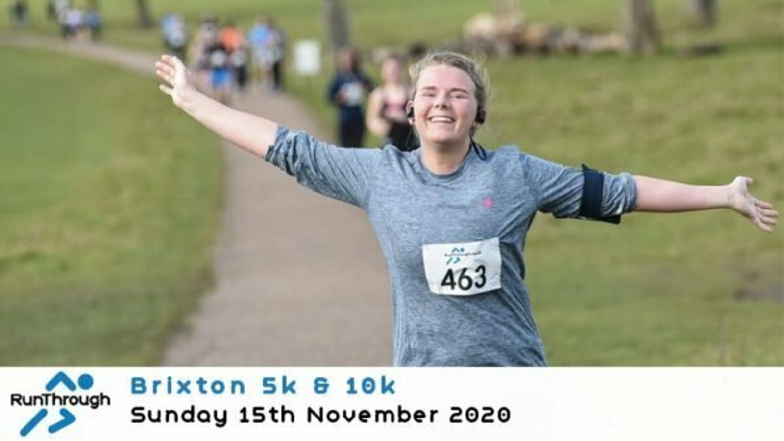 A person running outdoors with arms spread wide, wearing a gray long-sleeve shirt and race bib number 463. A group of people is seen in the background. Text reads: "RunThrough Brixton 5k & 10k Sunday 15th November 2020.