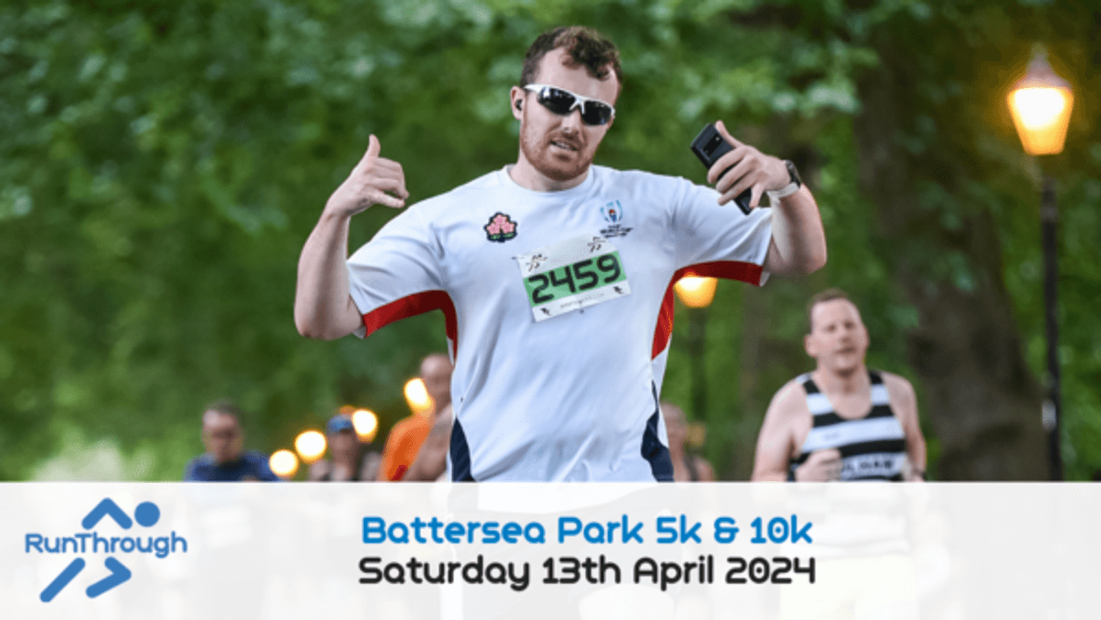 A man wearing a white shirt with a race bib number "2459" and dark sunglasses poses with thumbs-up during a run in a park. Other runners are seen in the background. The image promotes the "Battersea Park 5k & 10k" event taking place on Saturday, 13th April 2024.