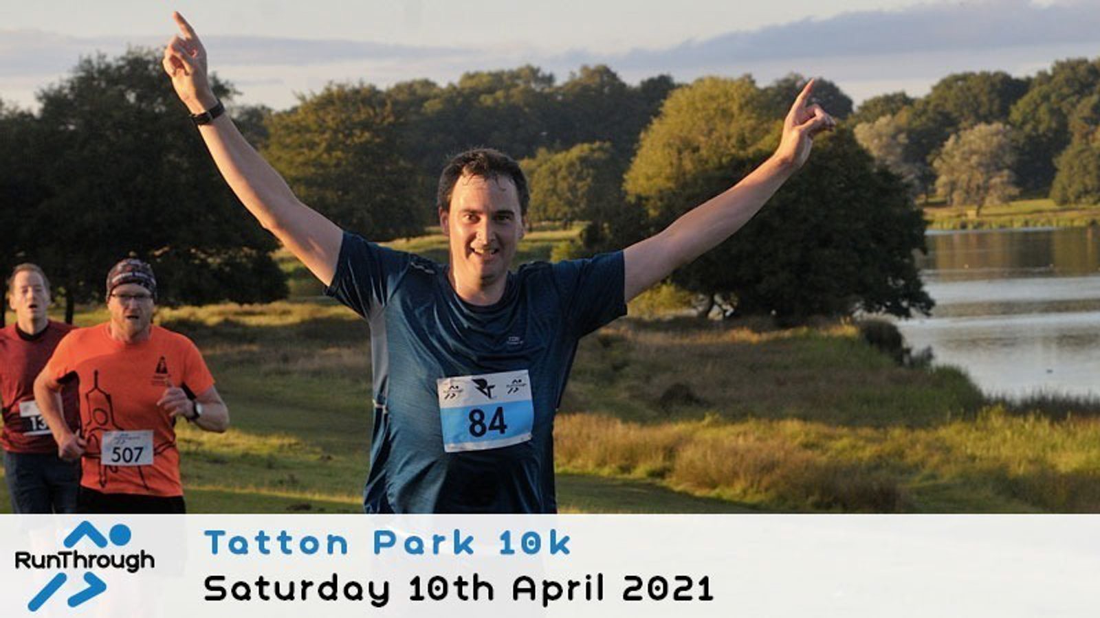 A man wearing a blue shirt and race bib 84 smiles with arms raised as he runs outdoors near a lake, with other runners behind him. Text reads: "Tatton Park 10k, Saturday 10th April 2021, RunThrough.