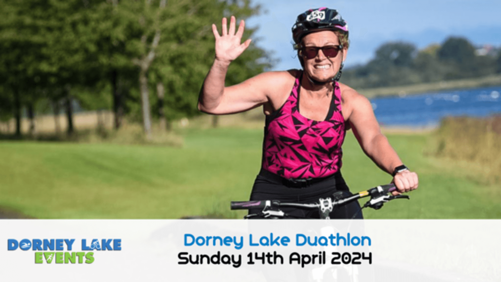 A person wearing a pink and black sleeveless top, sunglasses, and helmet rides a bicycle while smiling and waving. The event details on the image read "Dorney Lake Duathlon, Sunday 14th April 2024," with the Dorney Lake Events logo. The background shows a scenic lake.