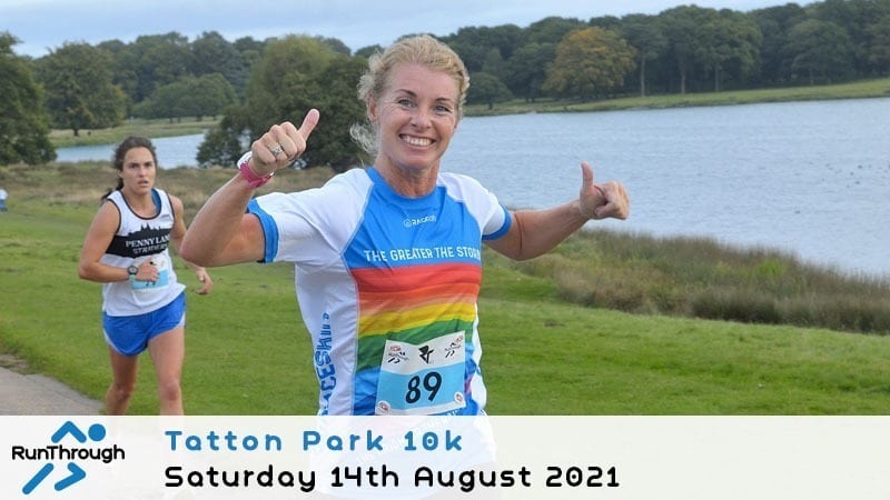 A smiling woman in a rainbow-themed running shirt gives a double thumbs-up while running a race near a lake. Another runner is behind her. Text at the bottom reads, "Tatton Park 10k, Saturday 14th August 2021.