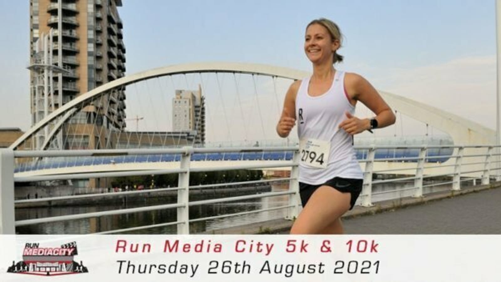 A woman wearing a white tank top and black shorts is jogging on a path near a river, with a bridge and buildings in the background. She has a race number "794" pinned to her outfit. The banner reads "Run Media City 5k & 10k, Thursday 26th August 2021.