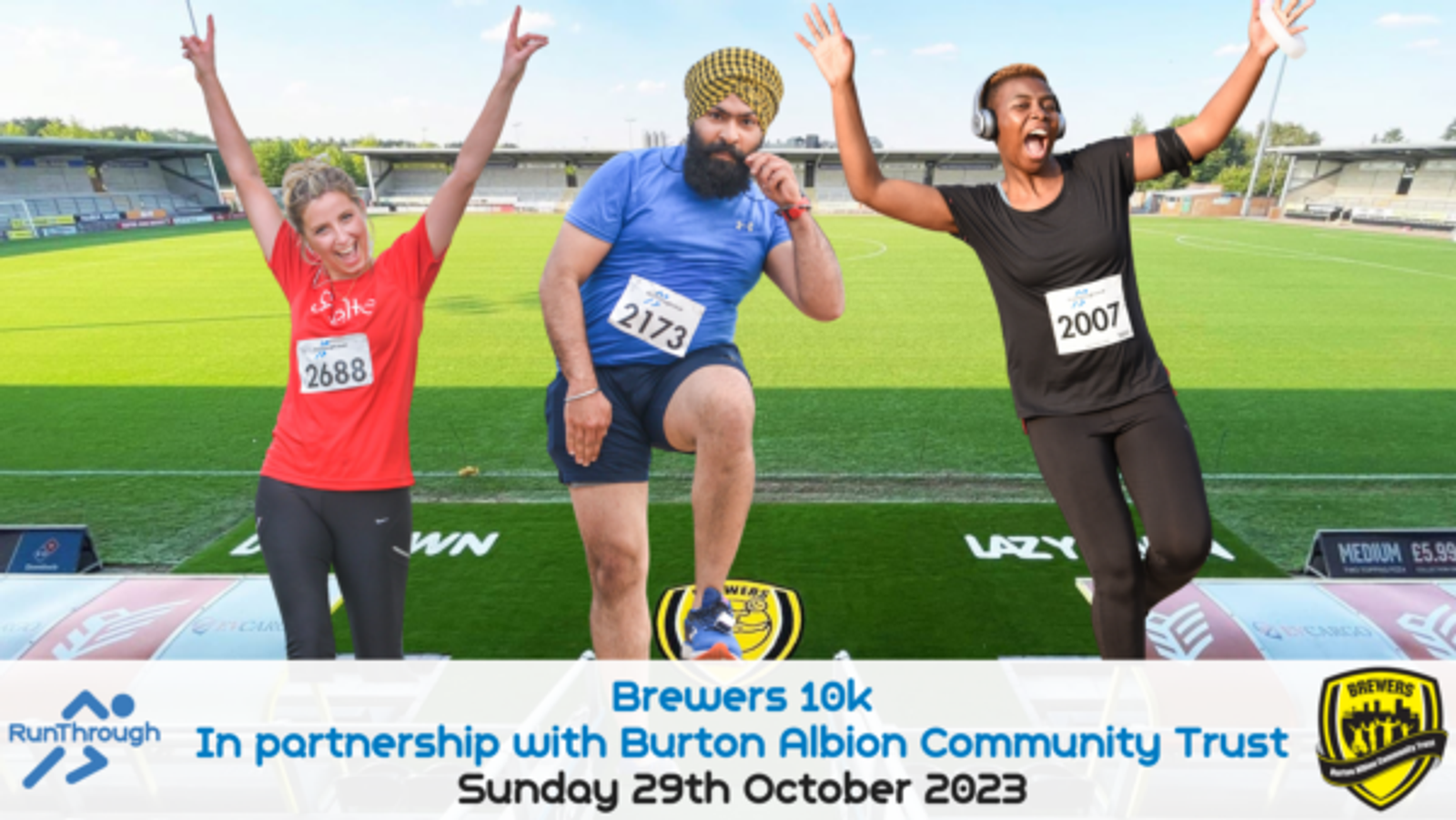 Three runners celebrate their achievement at a stadium finish line. Each wears a race bib (2688, 2173, 2007 respectively). They stand on podium blocks, smiling, with the Brewers 10k event details in front: Sunday 29th October 2023. Partnered with Burton Albion Community Trust.