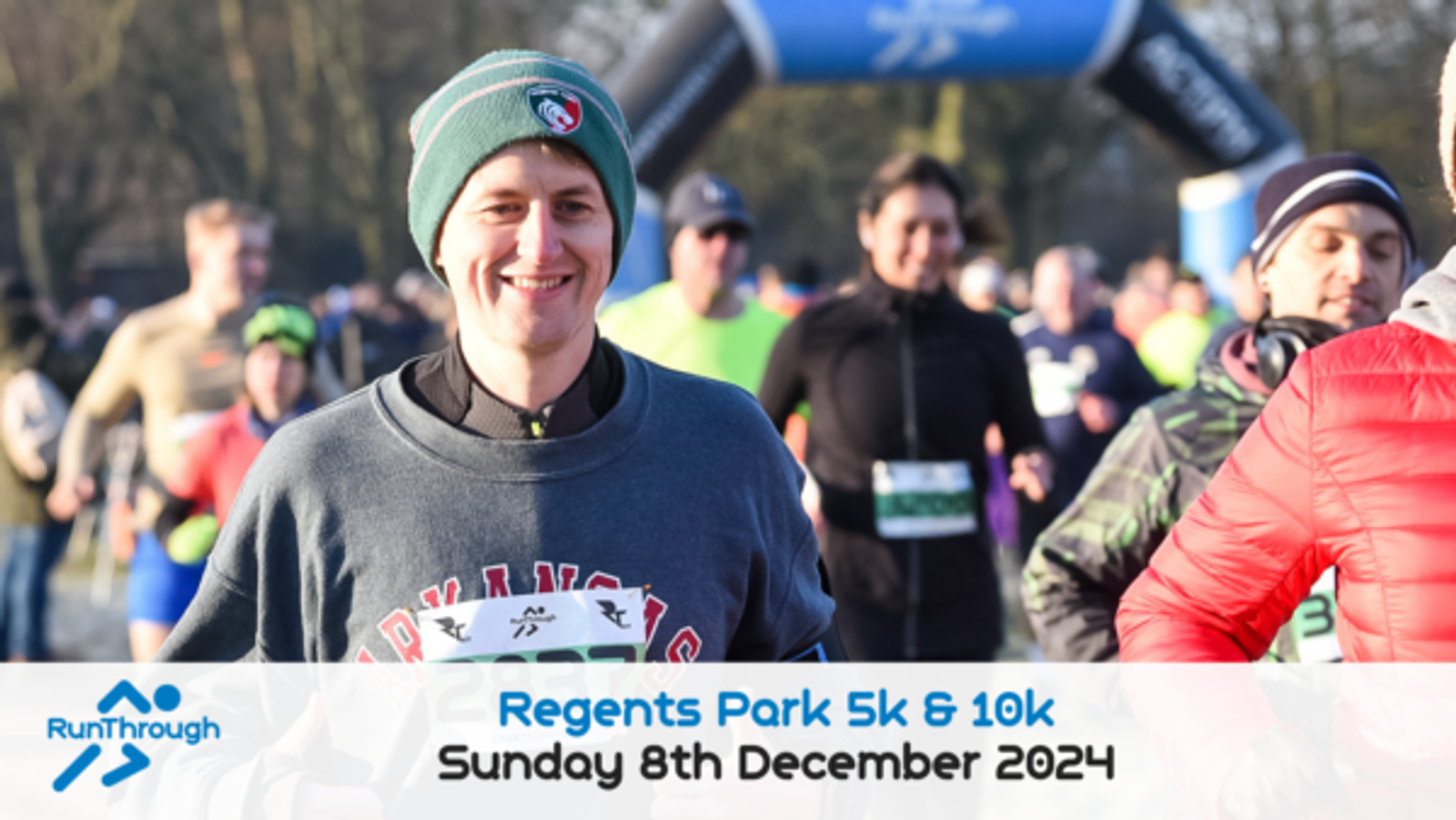 A man is running in a race, smiling at the camera. He wears a green beanie, a dark sweatshirt, and holds a piece of paper. Other runners are visible in the background. A banner at the bottom reads, "Regents Park 5k & 10k Sunday 8th December 2024." RunThrough logo included.