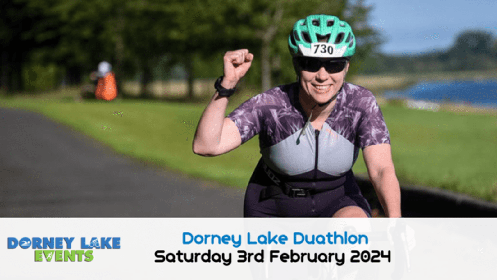 A cyclist with a green helmet and numbered "730" jersey raises her fist in celebration while riding along a paved path beside a lake. The image promotes the Dorney Lake Duathlon taking place on Saturday, 3rd February 2024. The logos and details are at the bottom.