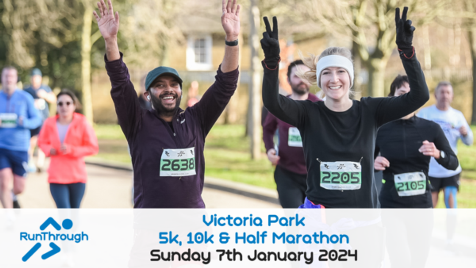 Runners smile and raise their arms in celebration during a race at Victoria Park. They are participating in the RunThrough 5k, 10k, & Half Marathon event scheduled for Sunday, January 7th, 2024, as noted on a banner in the foreground.