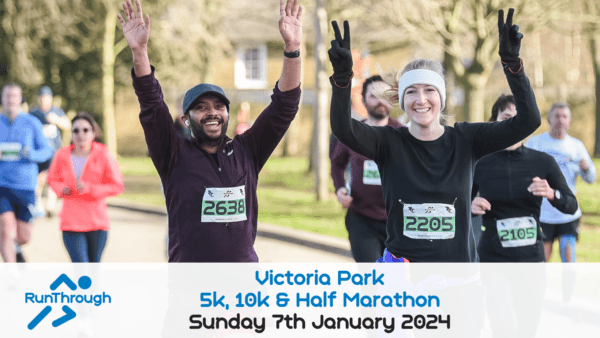 Runners smile and raise their arms in celebration during a race at Victoria Park. They are participating in the RunThrough 5k, 10k, & Half Marathon event scheduled for Sunday, January 7th, 2024, as noted on a banner in the foreground.