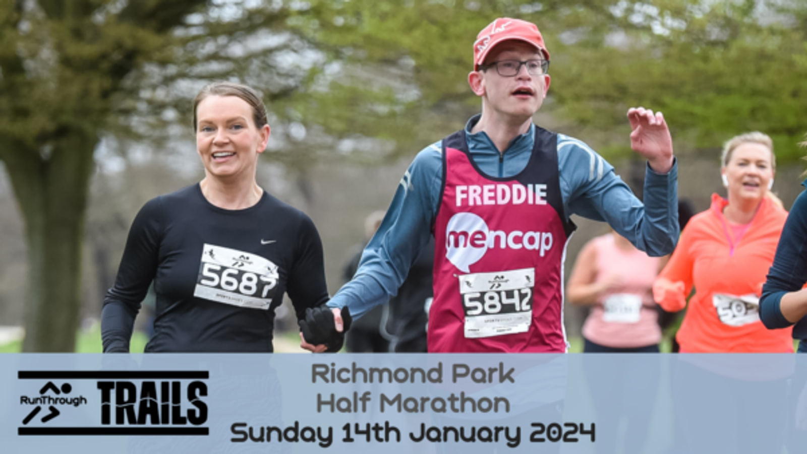 Runners participate in the Richmond Park Half Marathon on Sunday, 14th January 2024. A woman is running alongside a young man wearing a pink bib with the name "Freddie" and the Mencap logo, both smiling and appearing to enjoy the event.