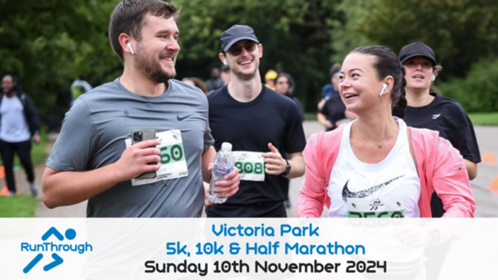 A group of runners participating in a race at Victoria Park, smiling and interacting with each other. The event includes a 5k, 10k, and Half Marathon, scheduled for Sunday, November 10th, 2024. The "RunThrough" logo is displayed on the left.