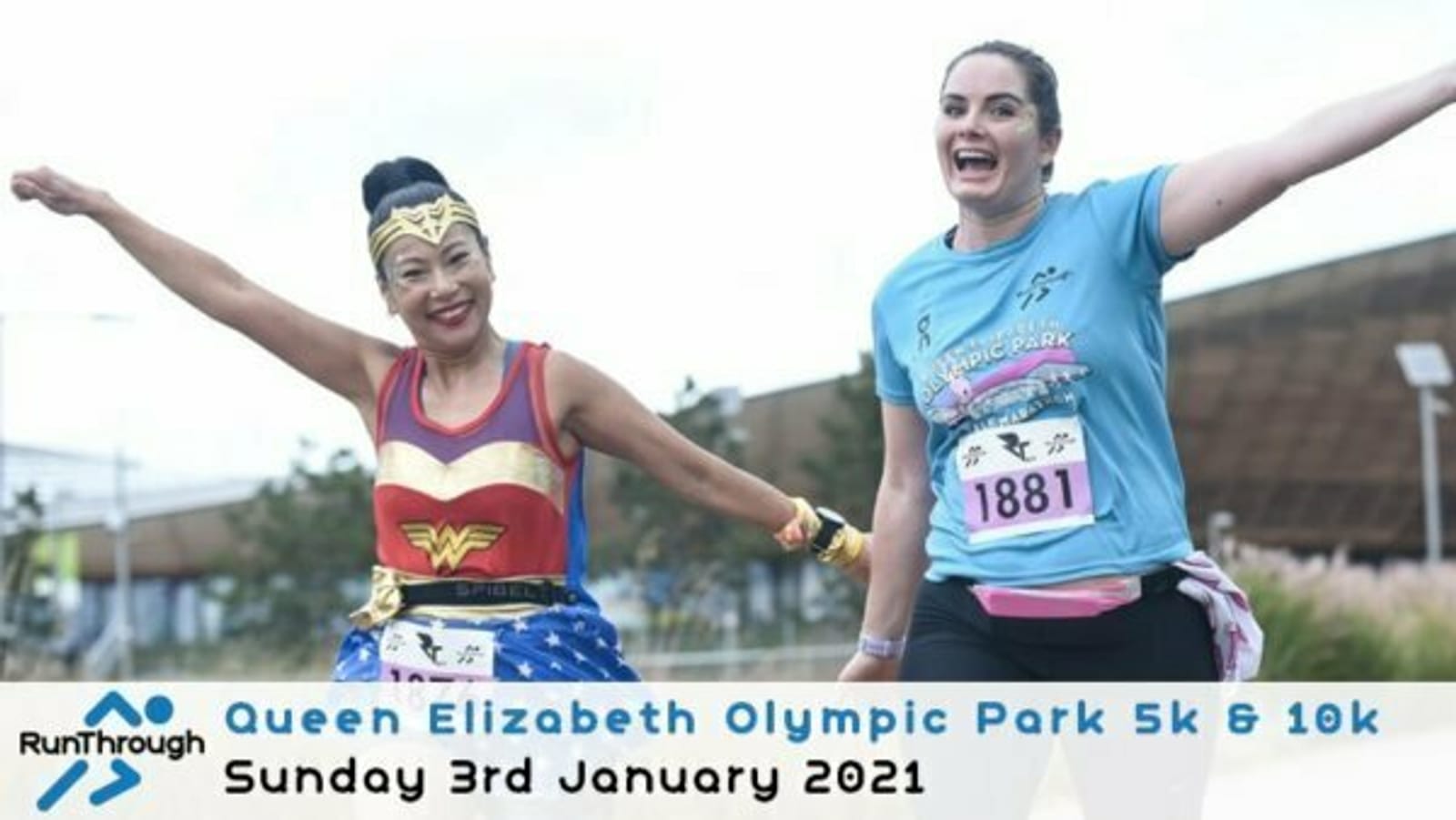 Two women joyfully running together at the Queen Elizabeth Olympic Park 5k & 10k event on January 3rd, 2021. One is dressed as Wonder Woman and the other in a blue shirt with colorful prints. Both are smiling with their arms extended outward. Event branding appears at the bottom.