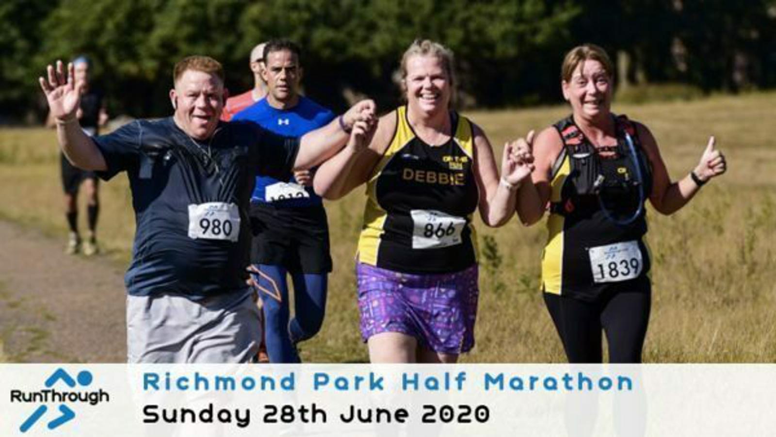Three runners are smiling and raising their arms in celebration as they participate in the Richmond Park Half Marathon. They are wearing numbered bibs and athletic gear. A sign at the bottom reads, "Richmond Park Half Marathon, Sunday 28th June 2020," with a logo on the left.