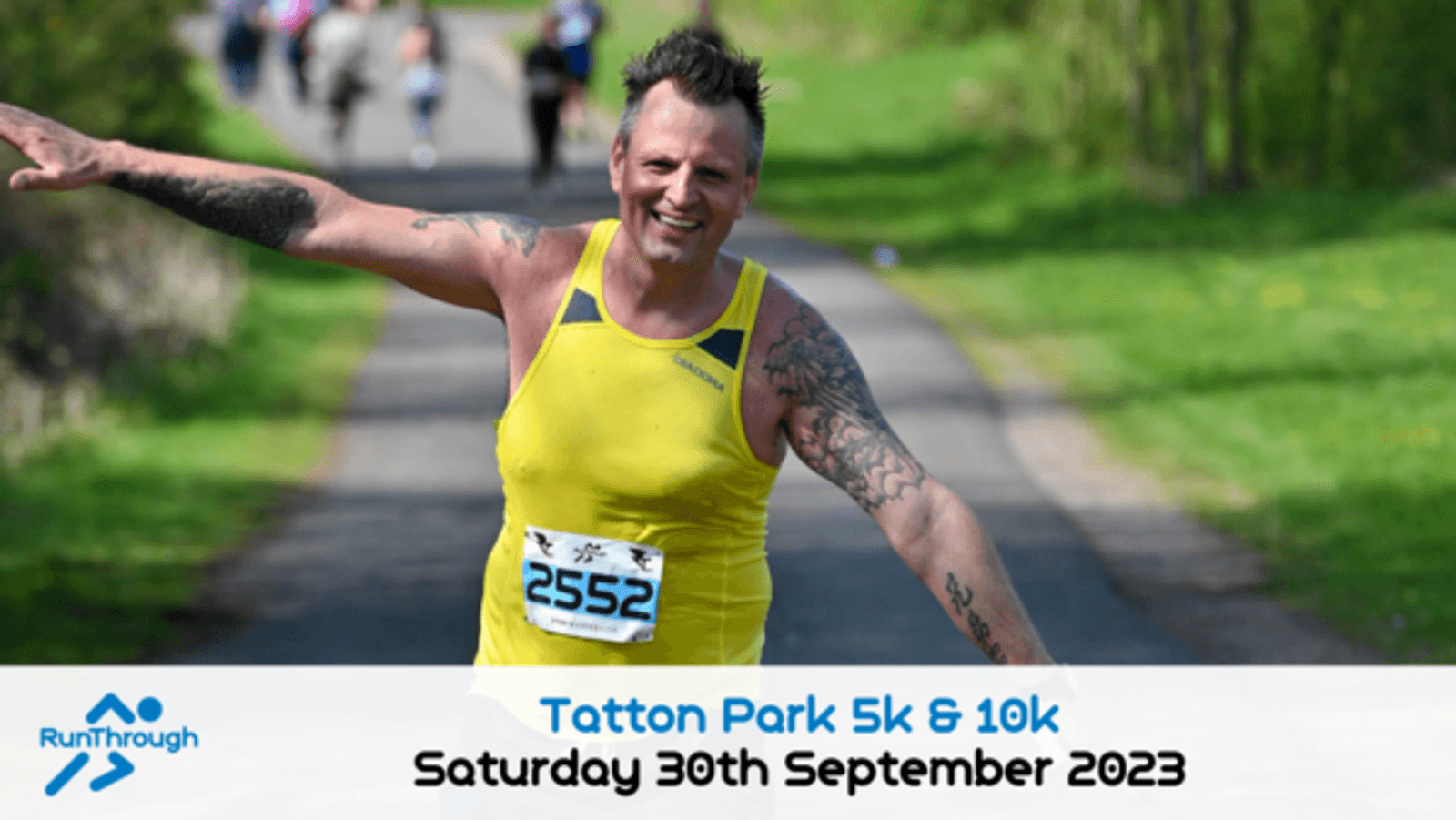 A smiling runner, wearing a yellow tank top and bib number 2552, spreads his arms wide as he runs on a path in a park during the Tatton Park 5k & 10k race. The event date, "Saturday 30th September 2023," is displayed at the bottom. The RunThrough logo is also visible.