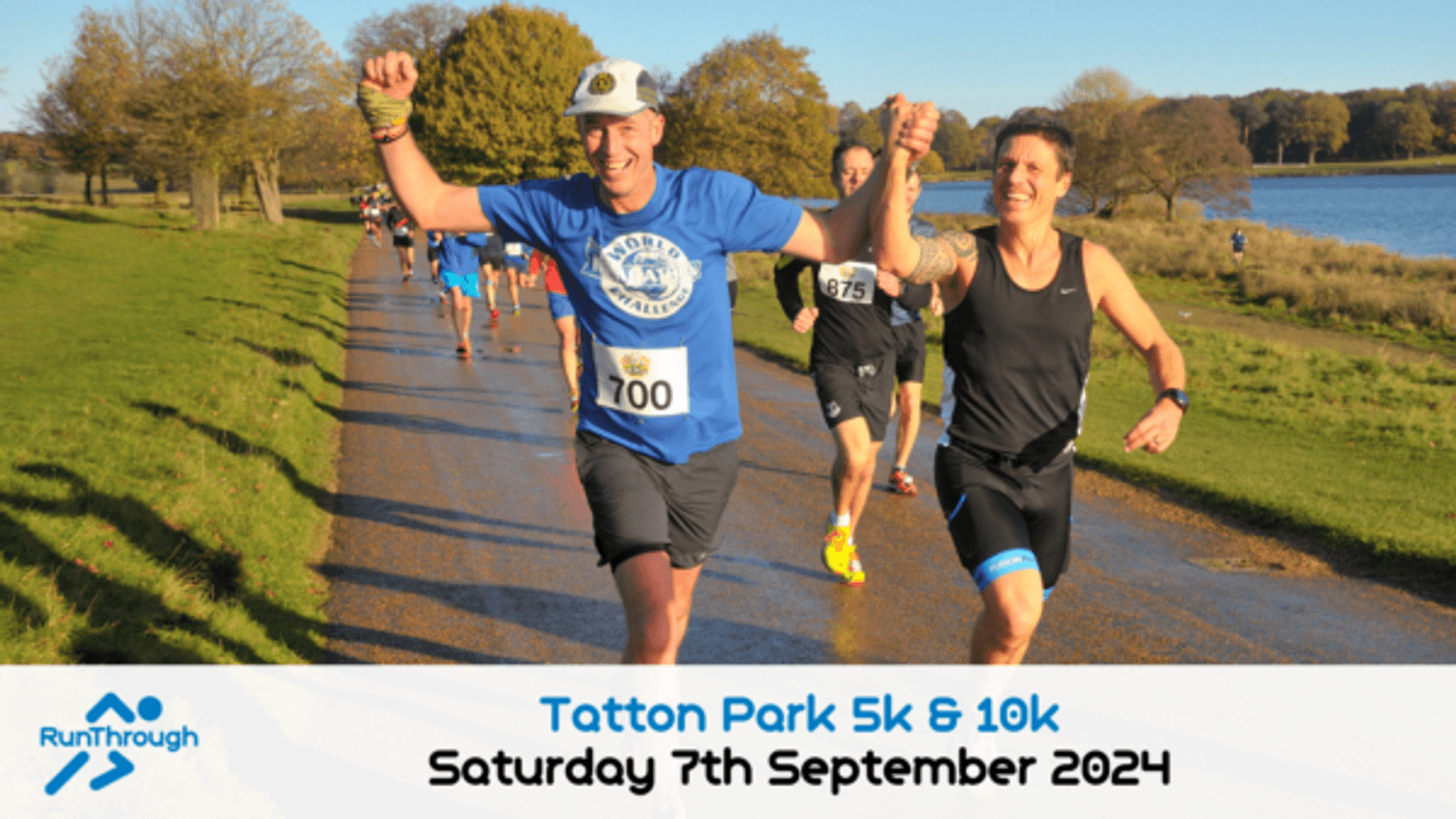 Runners on a park path participate in the Tatton Park 5k & 10k race. A man in a blue shirt with bib number 100 raises his arms in excitement next to another runner. Trees and a body of water are seen in the background. The event is scheduled for September 7, 2024.
