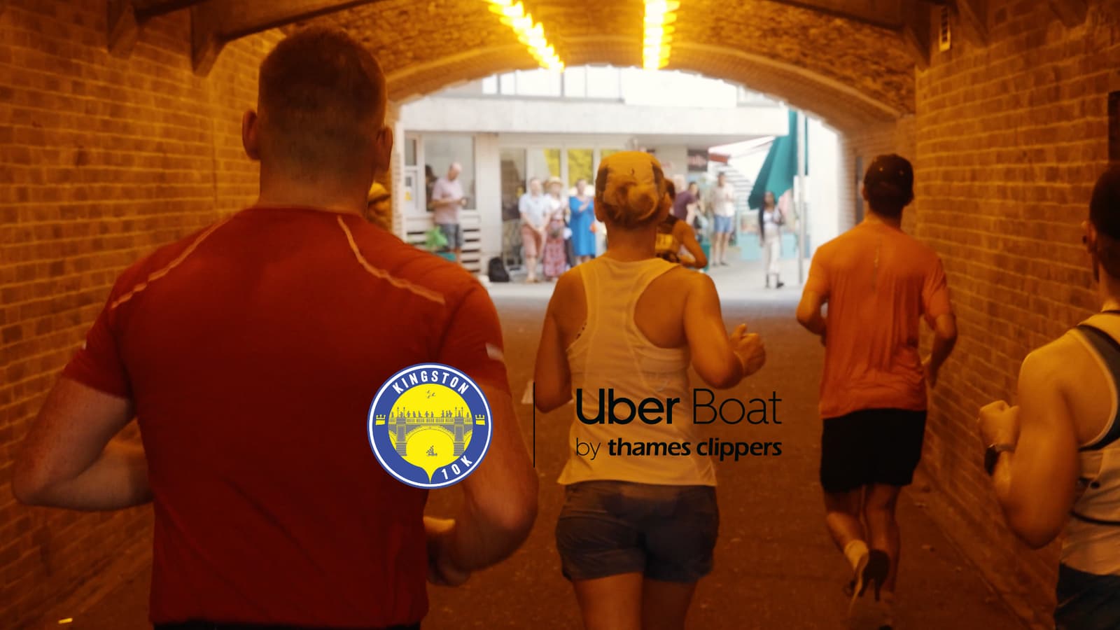 People participating in a run under a brick archway. The back of their shirts are visible, and an "Uber Boat by Thames Clippers" logo and a "Kingston 10k" logo are overlaid on the image. Spectators are visible in the background.