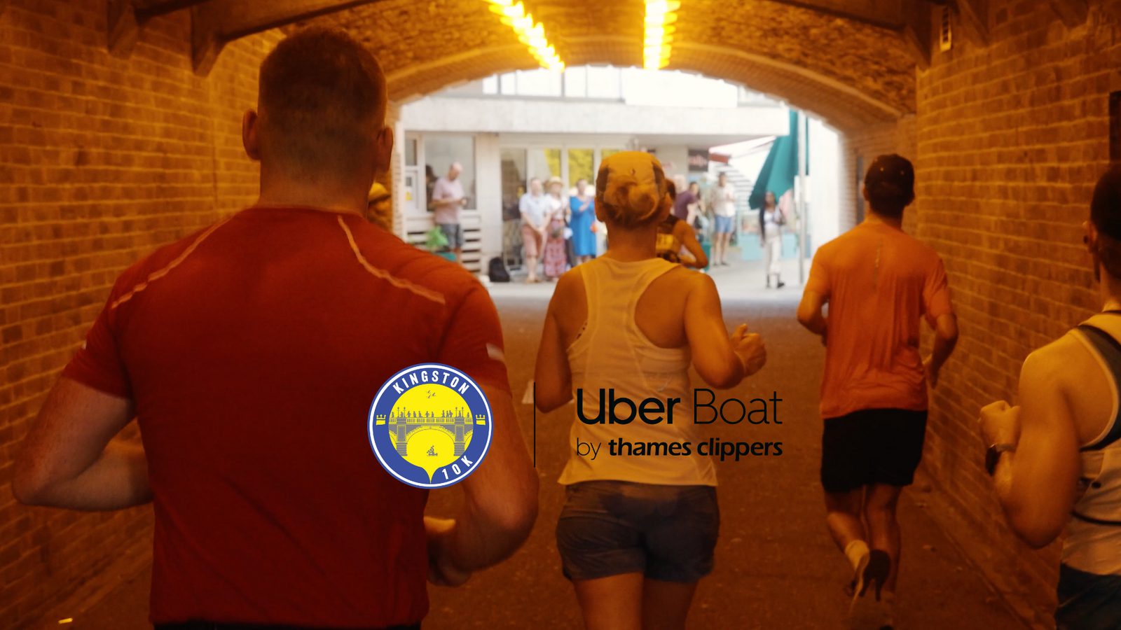 A group of runners jogs through a brick archway with a sign for "Uber Boat by Thames Clippers." The Kingston Run logo is visible on the left side of the image. In the background, more people and buildings are visible under the archway.