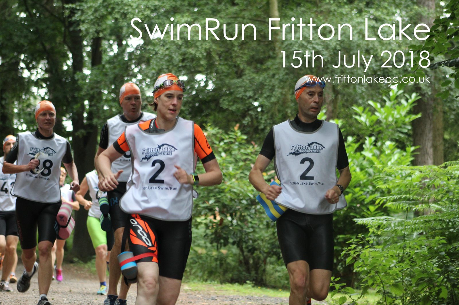 Participants in a SwimRun event at Fritton Lake on July 15th, 2018, run through a forested area. They wear orange swim caps and race bibs. The atmosphere is energetic and focused.