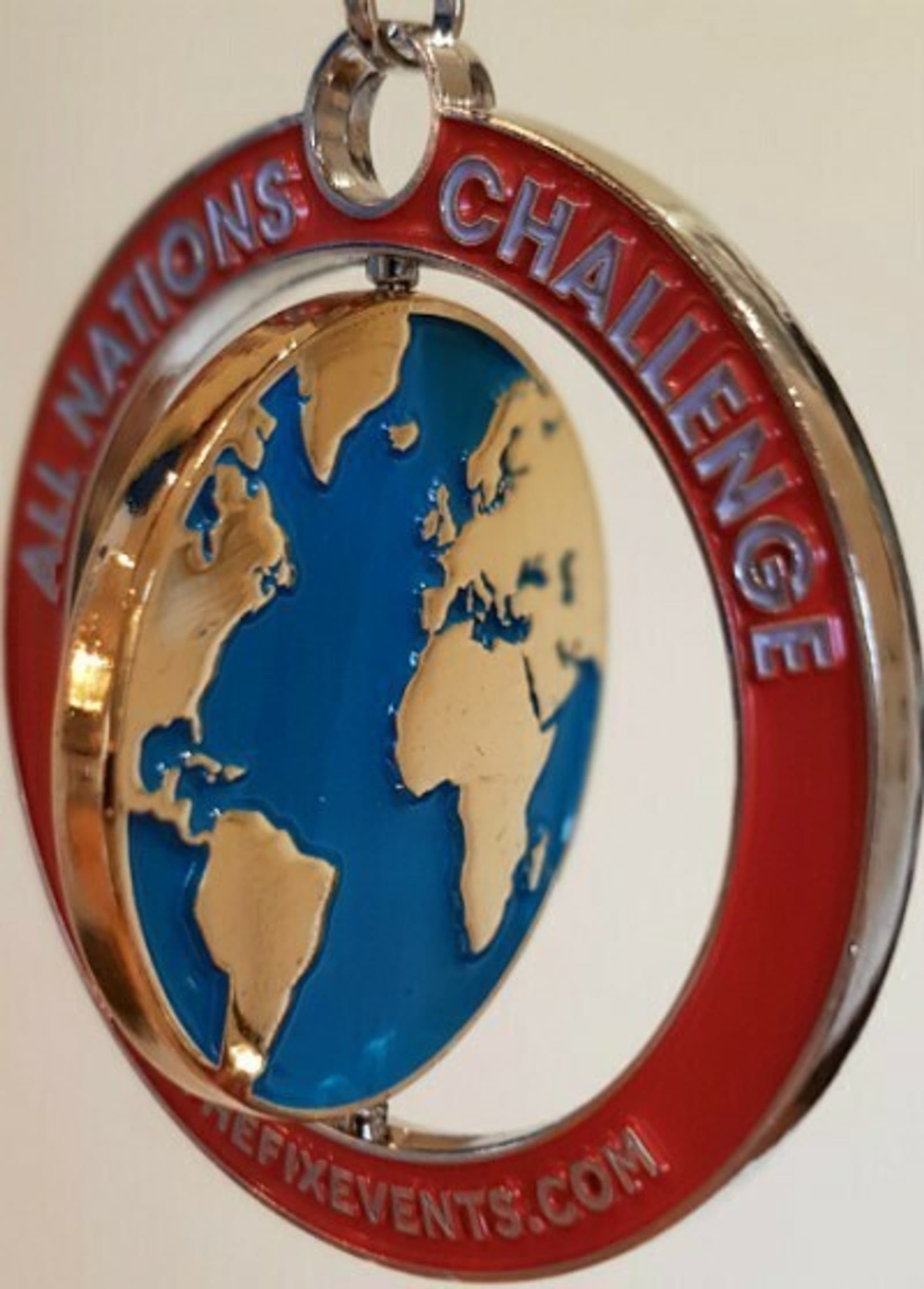 A medal with a blue and gold map of the world in the center. The outer ring is red with the words "ALL NATIONS CHALLENGE" inscribed on the top half, and the website "THEFIXEVENTS.COM" on the bottom half.