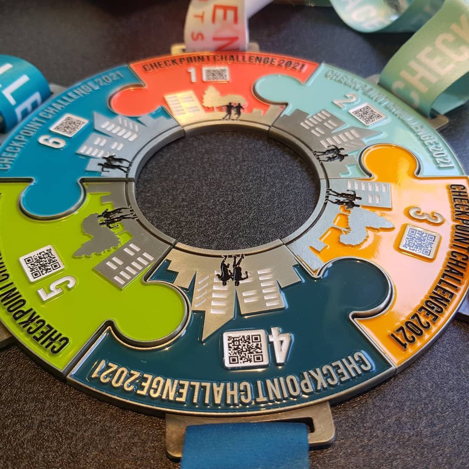 A circular medal designed to look like interconnected puzzle pieces, each piece numbered 1 through 6, representing different checkpoints of a 2021 challenge. The medal features QR codes and silhouettes of climbers, and is attached to a blue ribbon.