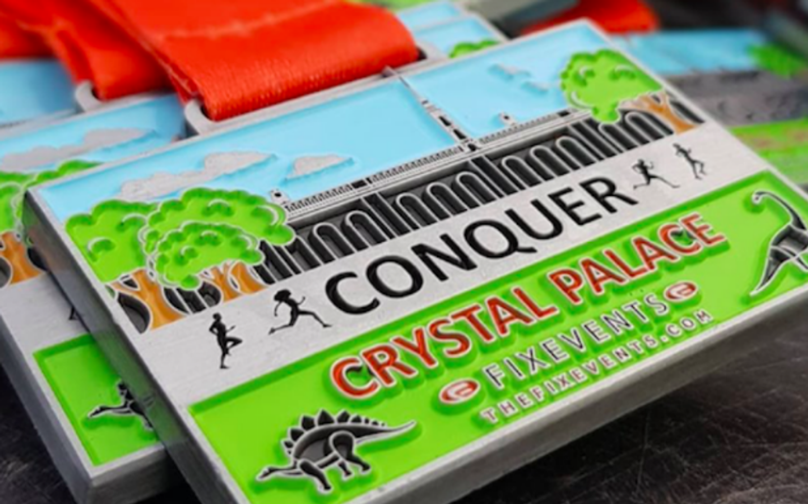 A colorful medal with a red ribbon reads "CONQUER CRYSTAL PALACE" on the front. The design includes a depiction of the Crystal Palace, silhouettes of runners, green trees, and illustrations of dinosaurs. The bottom features the logo and website for Fix Events.