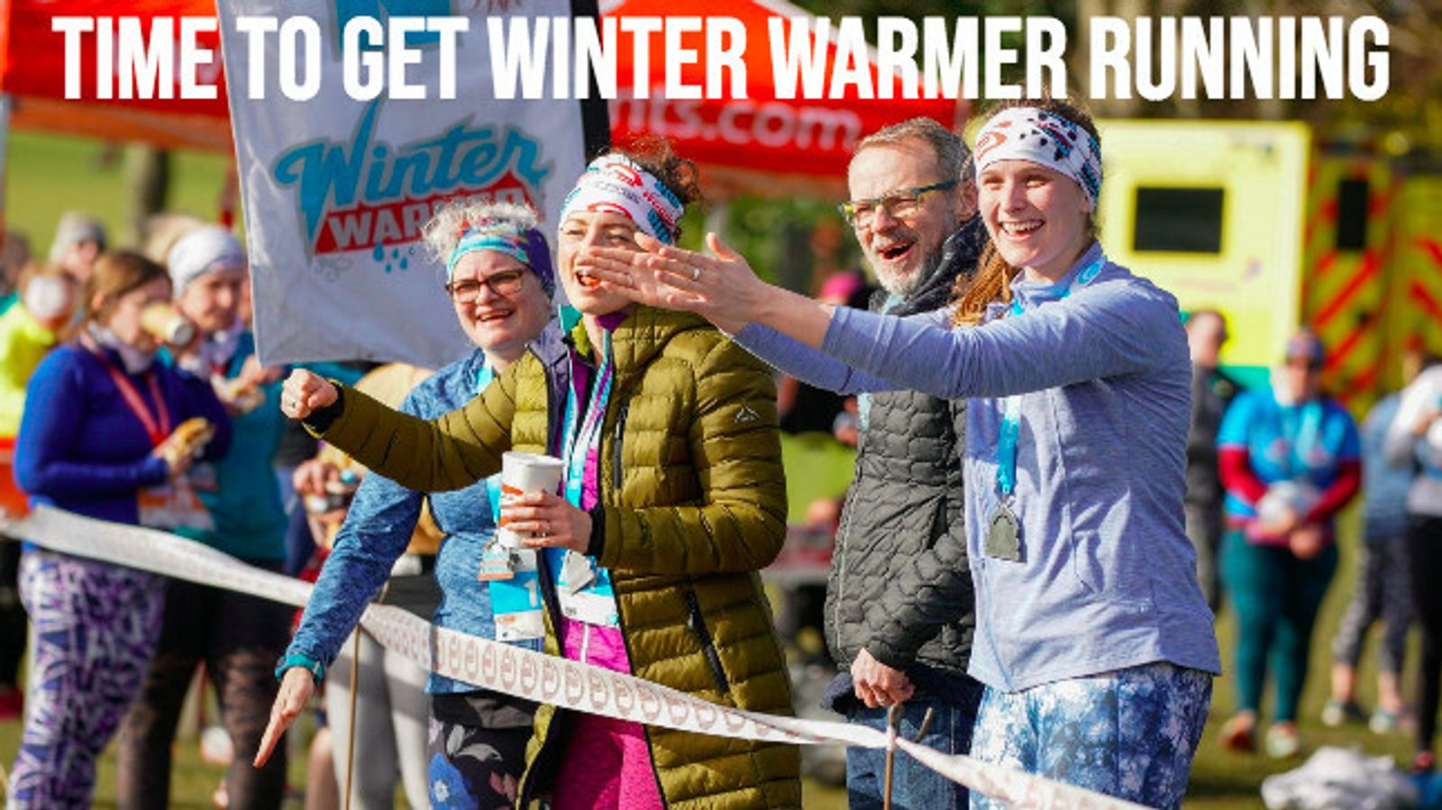 A group of cheerful people dressed in activewear and winter gear stand near a start line at an outdoor event. They are smiling and gesturing energetically, with "Time to Get Winter Warmer Running" written in bold white letters at the top of the image.