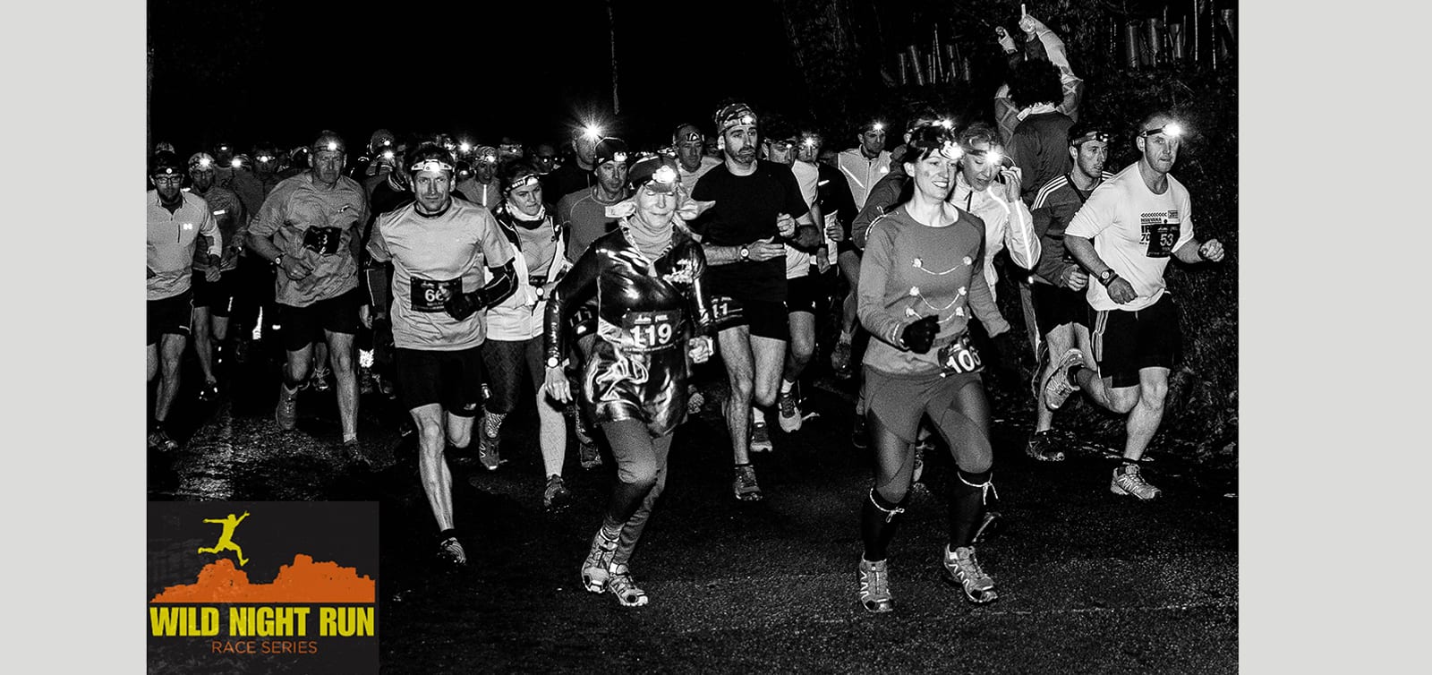 Black and white photo of a group of runners participating in a nighttime race wearing headlamps. The runners are dressed in athletic gear, jogging along a wet pavement. A banner in the bottom left corner reads "Wild Night Run Race Series.