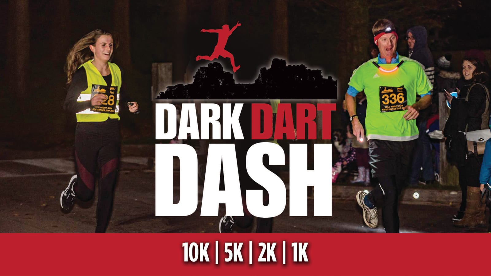 Two runners, a man and a woman, wearing race numbers and neon vests participate in a night race. The man wears a headlamp. Spectators cheer in the background. Text reads "Dark Dart Dash" with options for 10K, 5K, 2K, and 1K distances.