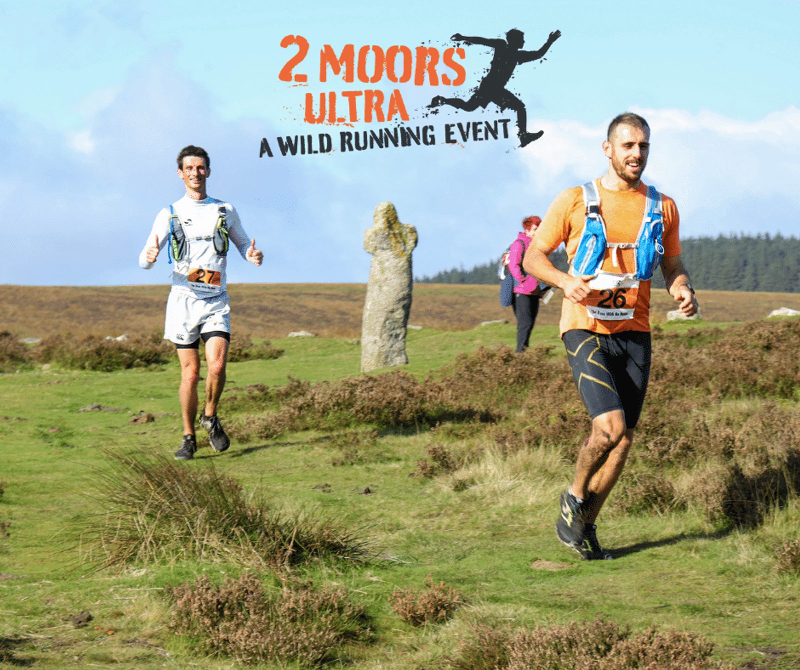 Two male runners with race numbers 27 and 26 on their shirts running on a grassy trail during the 2 Moors Ultra event. The runner in front is wearing an orange shirt and black shorts, while the second runner is wearing a white shirt and black shorts.