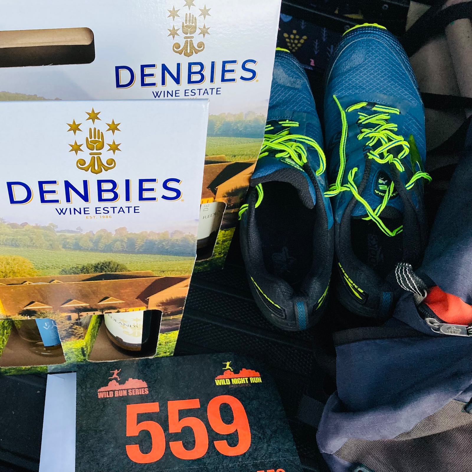 Running event supplies in a car, including a race bib with the number 559, a pair of blue running shoes with neon green laces, and two boxes of Denbies Wine Estate products.