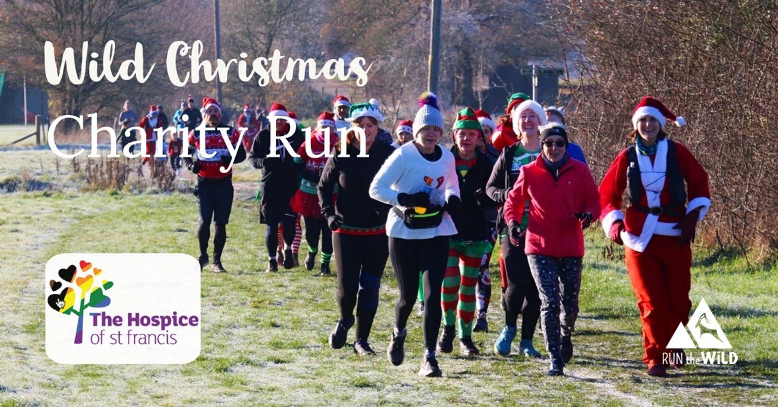 A group of people are running outdoors on a frosty path, some dressed in festive costumes. The image promotes the "Wild Christmas Charity Run." The Hospice of St Francis logo and the Run the Wild logo are visible in the bottom left and right corners, respectively.