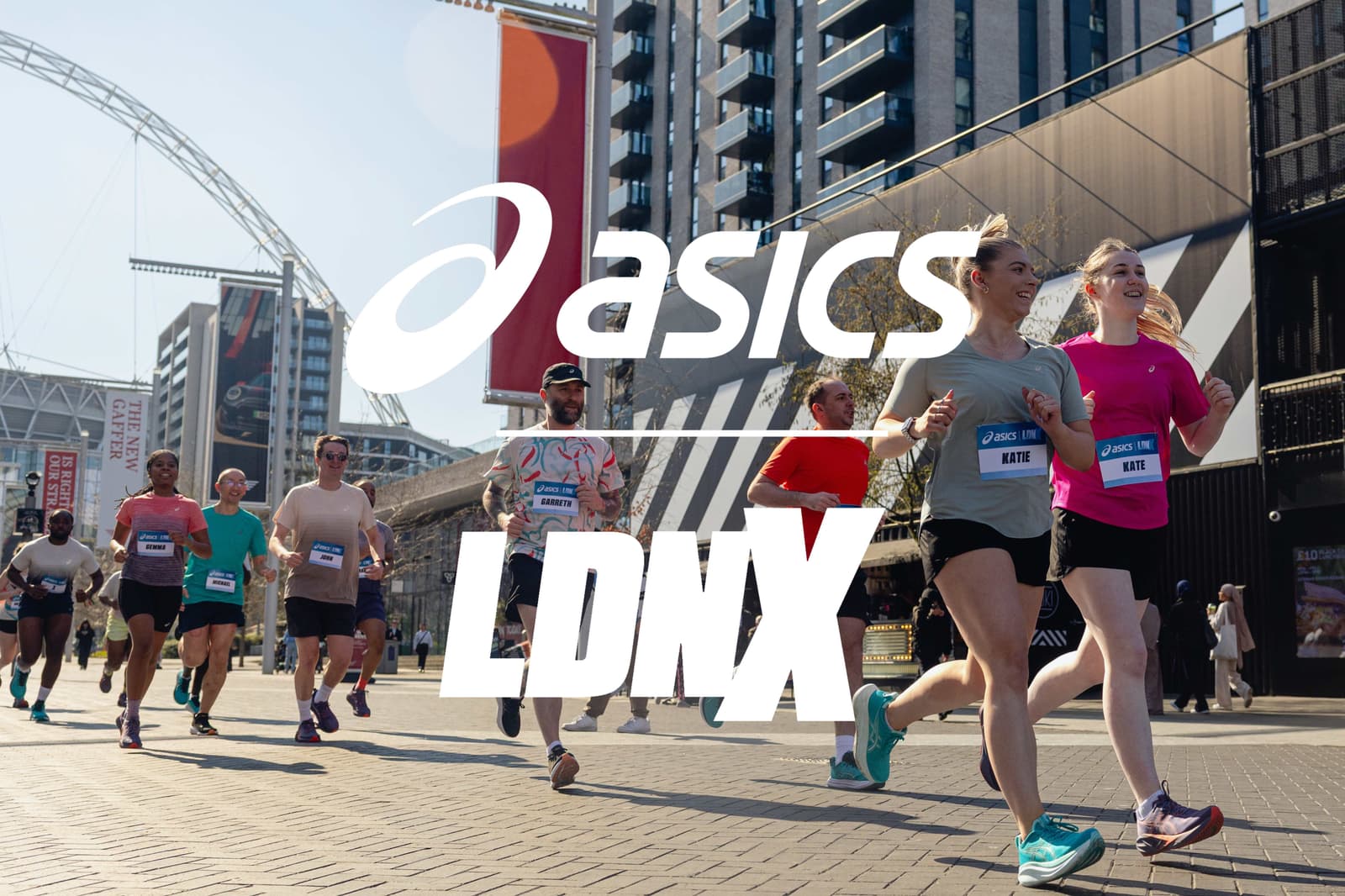 A group of people running on a city street during a race, with skyscrapers and a distinctive arch in the background. The image has large white text reading "asics LDNX" superimposed over the scene.