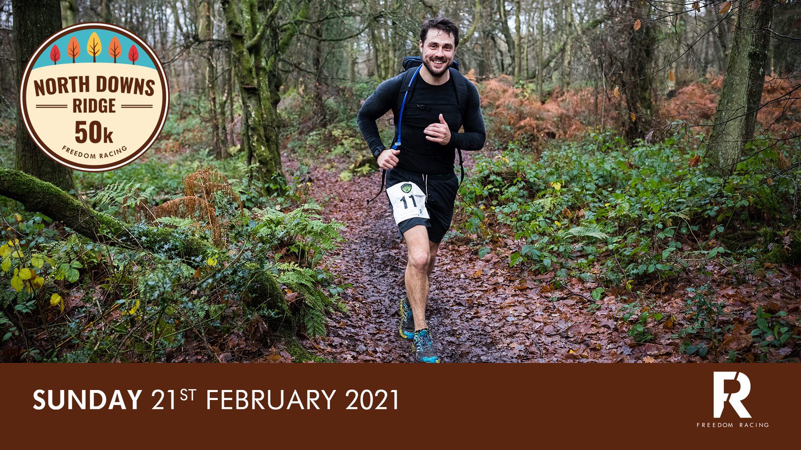 A runner wearing black athletic gear and race number 17 jogs through a forest trail during the North Downs Ridge 50k event. The setting is a moist, leafy forest with tall trees and autumnal foliage. The date "Sunday 21st February 2021" is displayed at the bottom.