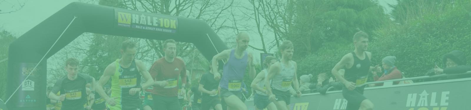 A group of runners are starting a race, passing under an inflatable archway labeled "Hale 10k." The participants are wearing athletic gear and race numbers. Trees and spectators are visible in the background, creating a lively atmosphere for the event.