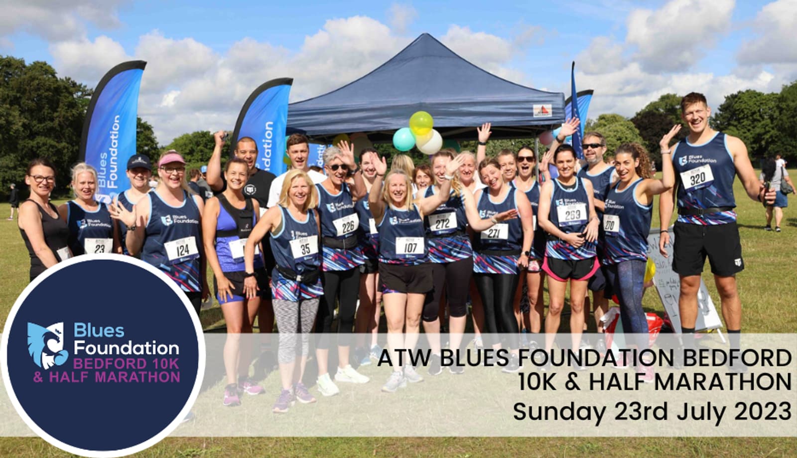 A group of runners, dressed in matching athletic jerseys, smile and raise their arms for a group photo near a tent. Various race bibs are visible. Text on the image reads "ATW Blues Foundation Bedford 10K & Half Marathon, Sunday 23rd July 2023.