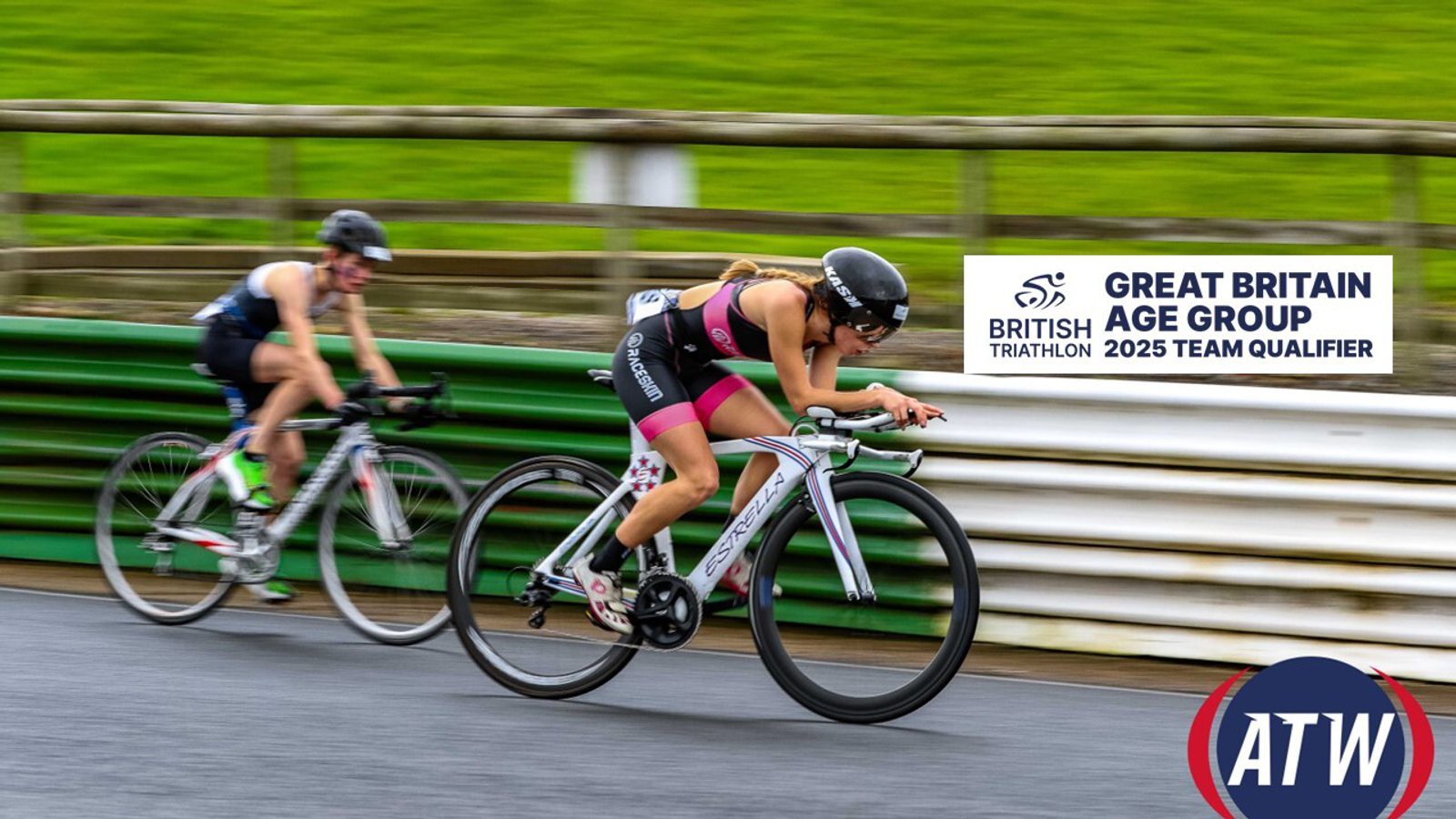 Two athletes compete in a cycling race on a road track, wearing helmets and triathlon gear. The graphic overlay reads "British Triathlon, Great Britain Age Group 2025 Team Qualifier." The track is bordered by green and white barriers with grass in the background.