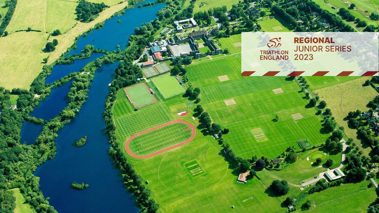 A scenic aerial view of a lush, green sports complex bordered by a river, showcasing multiple sports fields and tennis courts. A banner in the top-right corner displays the Triathlon England logo and reads "Regional Junior Series 2023".