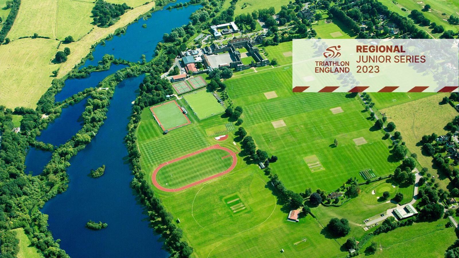 A scenic aerial view of a lush, green sports complex bordered by a river, showcasing multiple sports fields and tennis courts. A banner in the top-right corner displays the Triathlon England logo and reads "Regional Junior Series 2023".