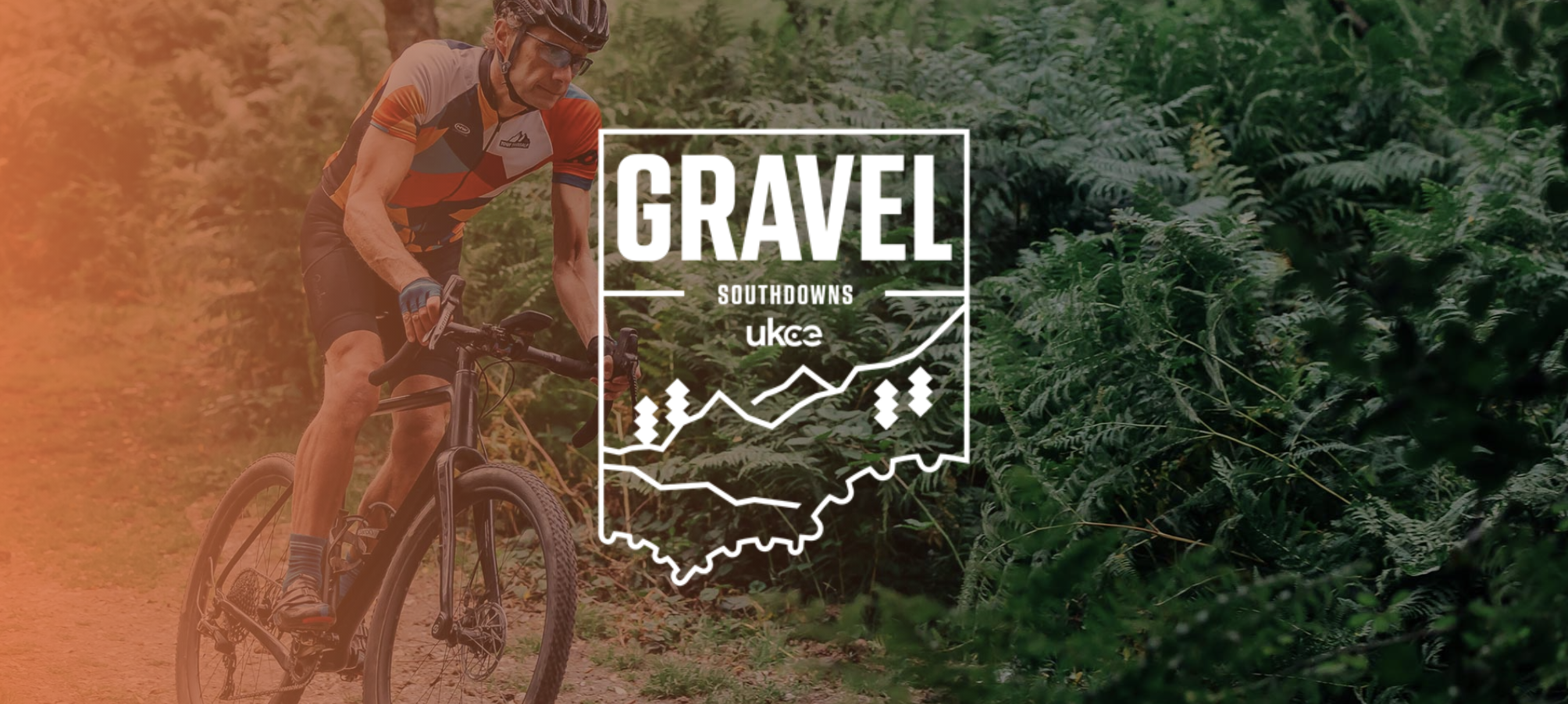 A cyclist wearing a helmet and sports attire rides a gravel bike on a dirt path through lush green ferns. The image has an overlay featuring the event name "Gravel Southdowns" and the UKCE logo at the center.