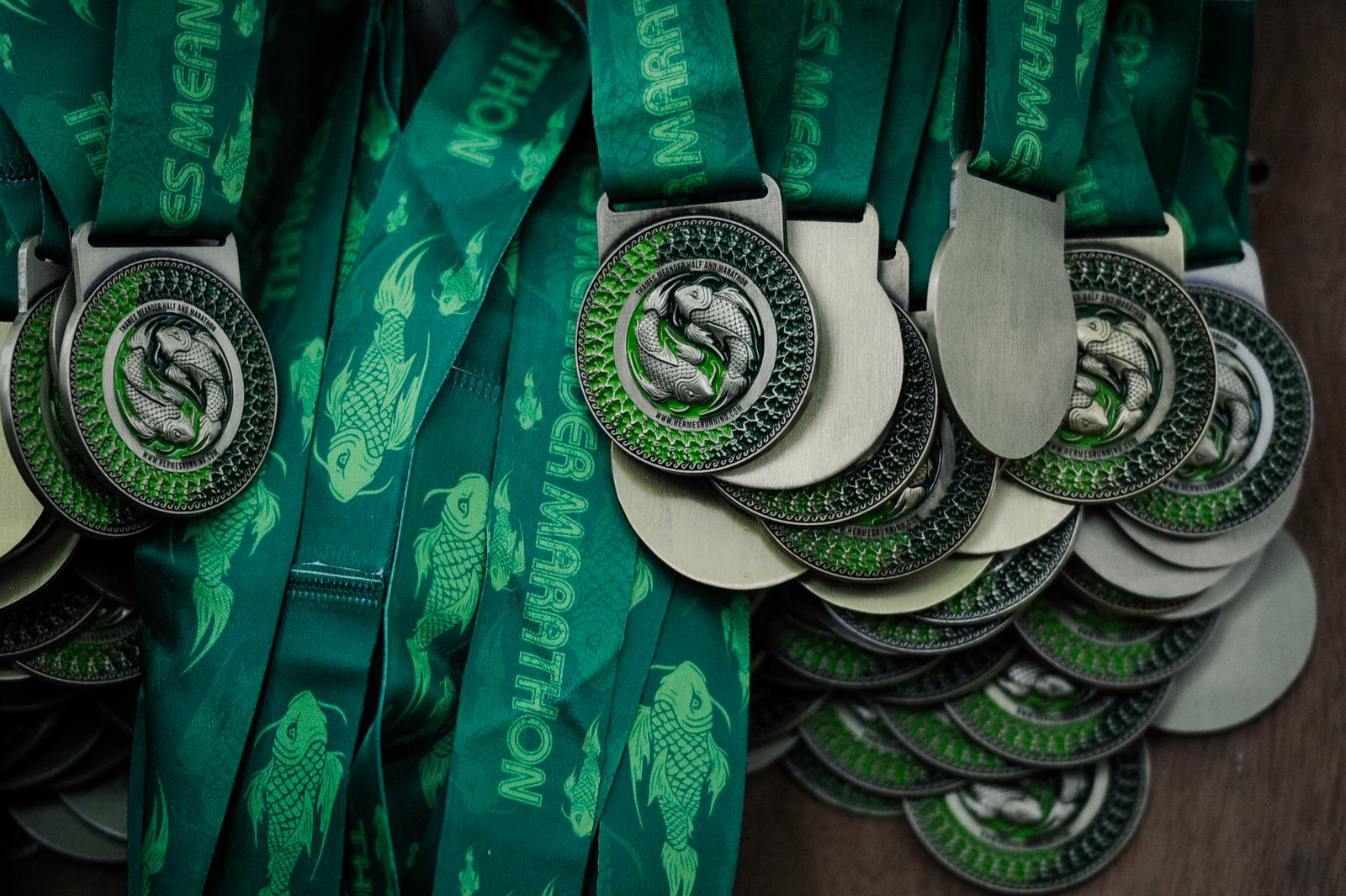 Close-up of a stack of green and silver medals featuring a fish design on the ribbons and the medal face. The medals are arranged in a pile, showcasing their intricate details and the event branding on the ribbons.