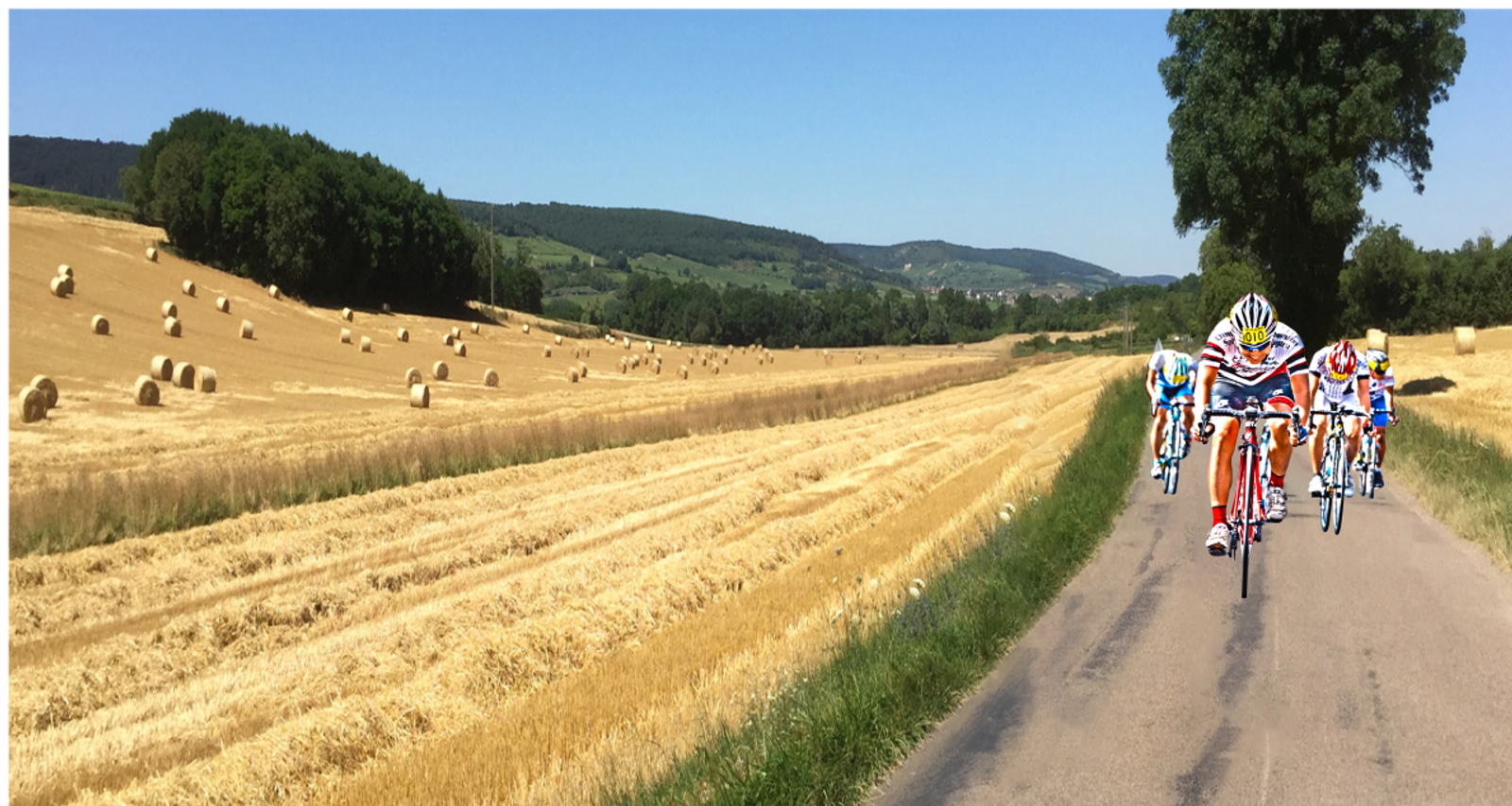 A group of cyclists in colorful racing gear rides along a narrow road through a picturesque countryside with harvested fields and scattered hay bales. Green hills and trees line the background under a clear blue sky.