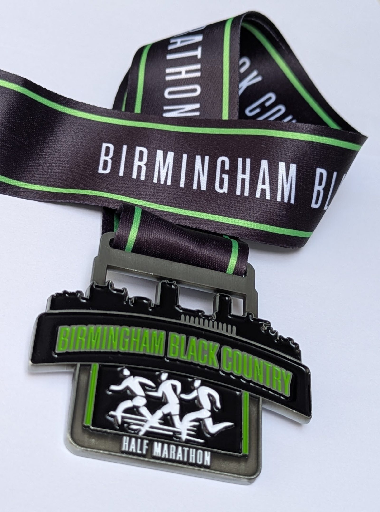 A Birmingham Black Country Half Marathon medal with three running figures and a black and green ribbon that reads "Birmingham Black Country.