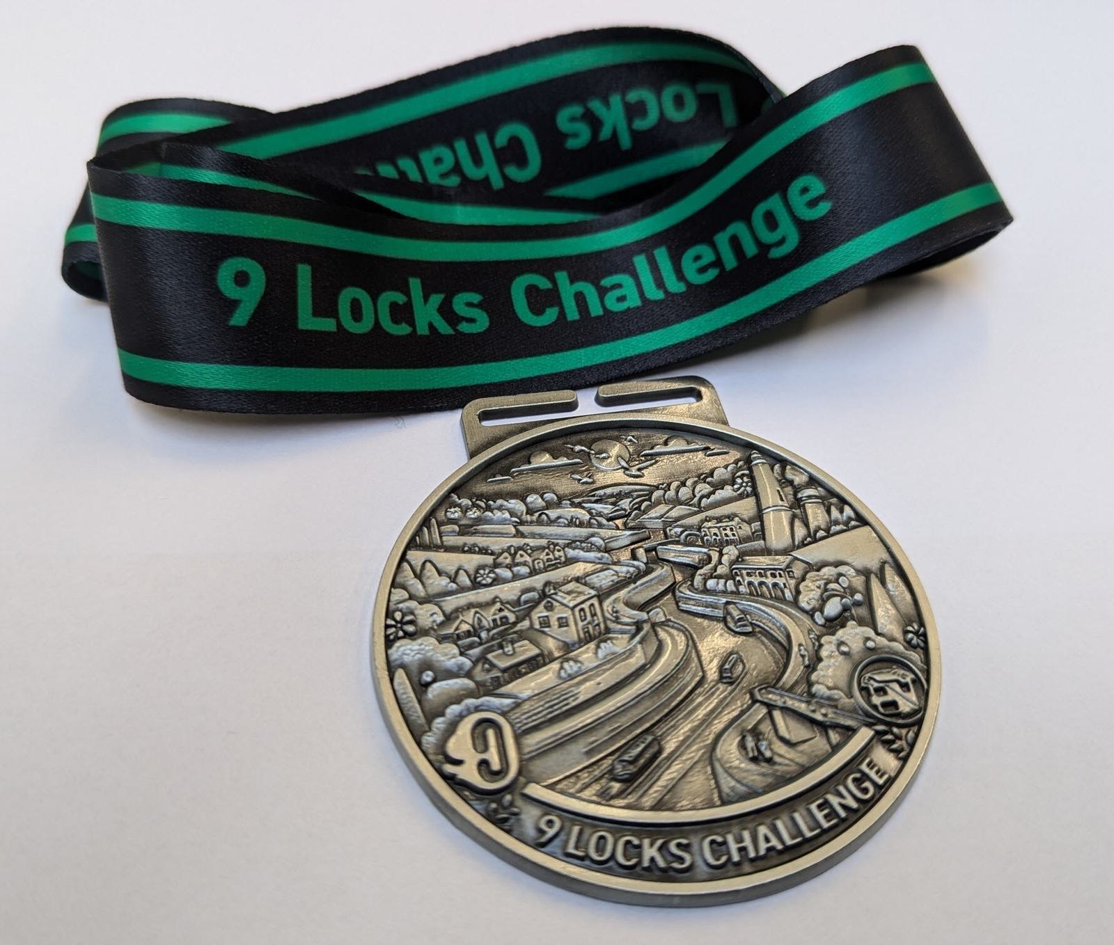 A silver medal with intricate imagery of a canal and locks, imprinted with "9 Locks Challenge." It hangs on a green and black ribbon with the same wording.