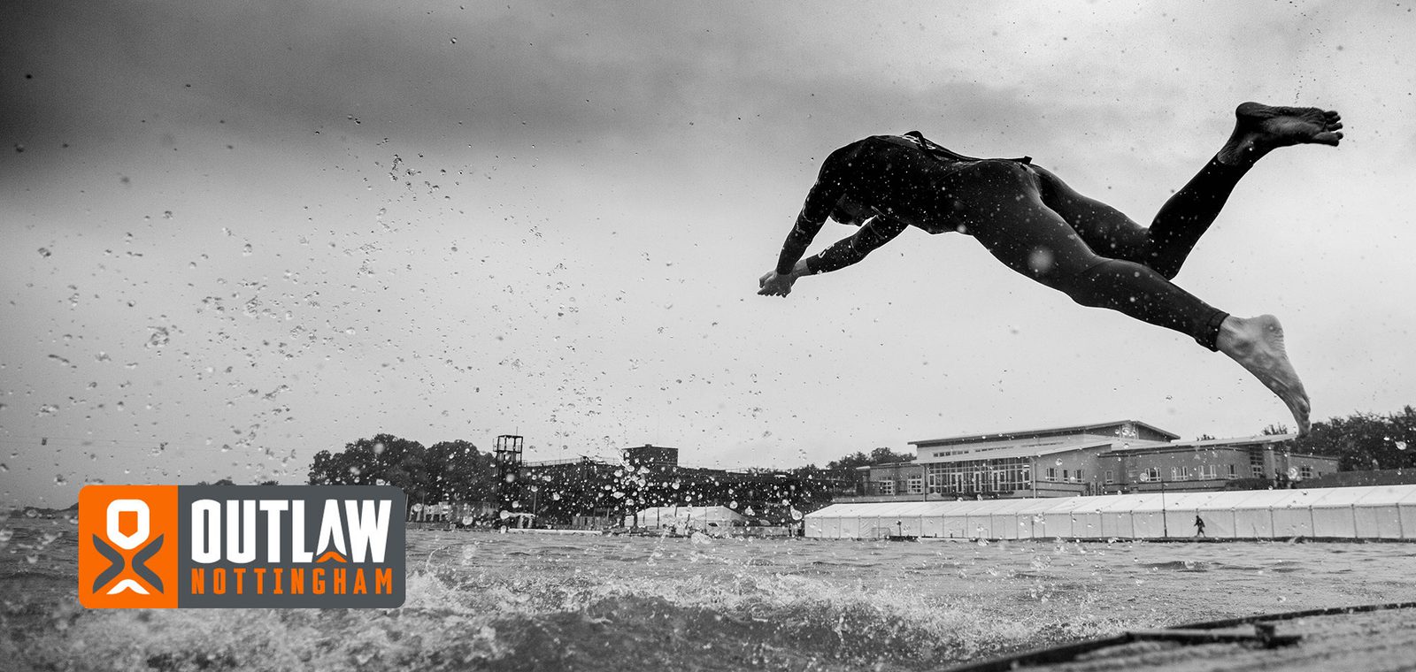 A person in a wetsuit dives into a body of water under a cloudy sky. Splashes of water are visible, and a large building stands in the background. The "Outlaw Nottingham" event logo is present in the lower left corner.